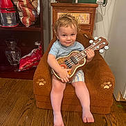 William joined the competition — help win amazing prizes! child, toddler, guitar, ukulele, musical_instrument, sitting, armchair, smiling, portrait, indoor, home, wooden_floor, shelves, shelf, clothing, shorts, barefoot, blond_hair, cozy, rock_star