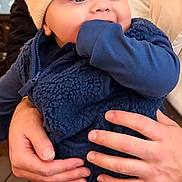 Otis joined the competition — help win amazing prizes! baby, child, blue_clothing, pom_pom_hat, hand, cheeks, face, sleeve, warm_clothing, adult_hands, indoor, soft_lighting, cozy, winter_hat, cute, portrait, young_child, holding, knit_hat, socks