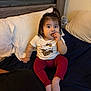 Kiara is registered to the contest to win money with this photo: bed, blanket, casual, child, clothing, cookie, cozy, cute, eating, furniture, hair, headboard, indoor, person, pillow, relaxing, socks, toddler, toy, wood