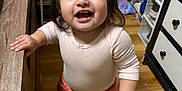 Kiara is registered to the contest to win money with this photo: baby, barefoot, cabinet, child, clothing, face, furniture, hair, hand, happy, indoor, person, room, shelf, smiling, standing, storage, toddler, toy, wooden_floor