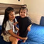Kiara is registered to the contest to win money with this photo: barefoot, bed, black_clothing, blue_bedsheet, child, cushion, family, hair_tie, happy, home, indoor, long_hair, playing, room, sitting, smiling, standing, wall_decor, white_tshirt, wooden_headboard