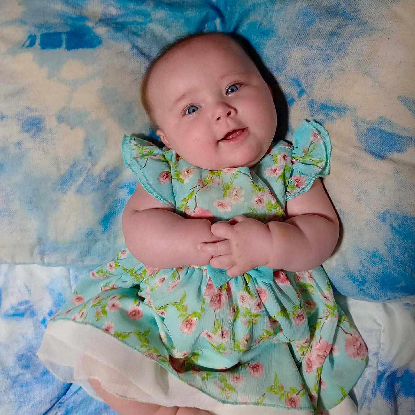Olivia joined the competition — help win amazing prizes! baby, blanket, blue_eyes, child, chubby_cheeks, closeup, cute, dress, feet, floral_pattern, hands, happy, indoors, infant, lying_down, pastel_colors, portrait, skin, smiling, soft_texture