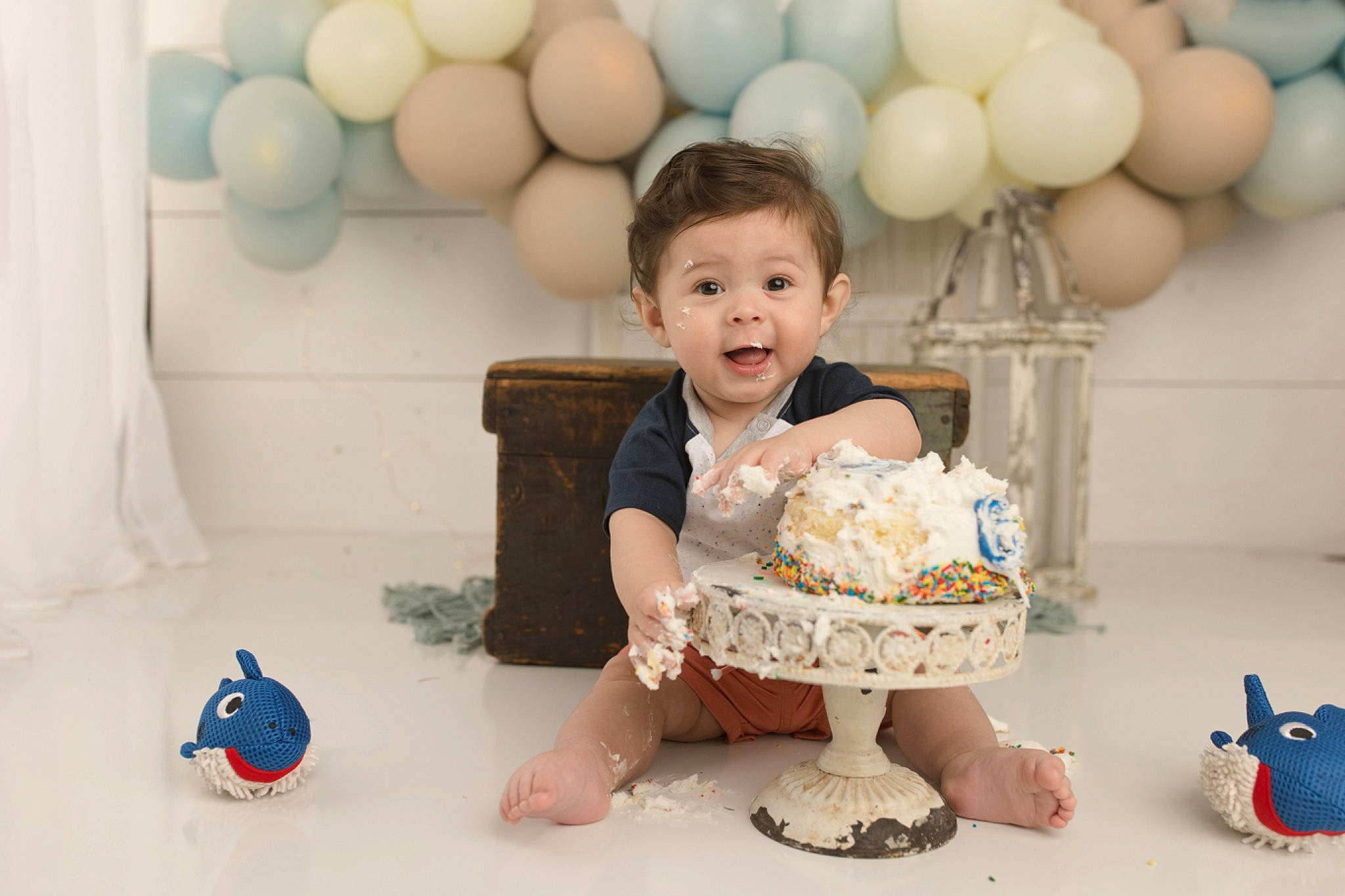 Aron is registered to the contest to win money with this photo: baby, baby_toddler_clothing, balloon, birthday, blue, child, dress, event, facial_expression, fun, happy, icing, party_supply, person, product, sitting, skin, smile, sweetness, toddler