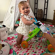 Maëlys participe au concours pour gagner de l'argent avec cette photo : toddler, baby_walker, indoor, play_mat, teepee, toy, child, smiling, happy, floor, colorful, footwear_free, tattoo, adult_hand, cushion, carpet, furniture, window, person, room