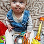 baby, child, blue_eyes, denim_overalls, polka_dot_shirt, tongue_out, toy, silver_ball, orange_crab_toy, colorful_toys, blanket, patterned_blanket, cute, indoor, playful, sitting, face, hand, expression, infant