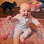 baby, child, infant, pajamas, quilt, floor, cat, pet, smiling, happy, indoors, playtime, cute, person, seated, soft_lighting, home, cozy, blanket, animal