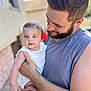 affection, arm, baby, background_blur, beard, blue_eyes, casual_clothing, child, daylight, family, flower, happy, holding, love, man, outdoor, parent, portrait, skin, sleeveless_shirt