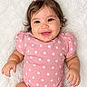 arms, baby, blanket, bow, child, close_up, daisies, face, floral_pattern, hair_bow, hands, happy, indoors, infant, lying_down, photography, pink_outfit, portrait, smiling, white_background