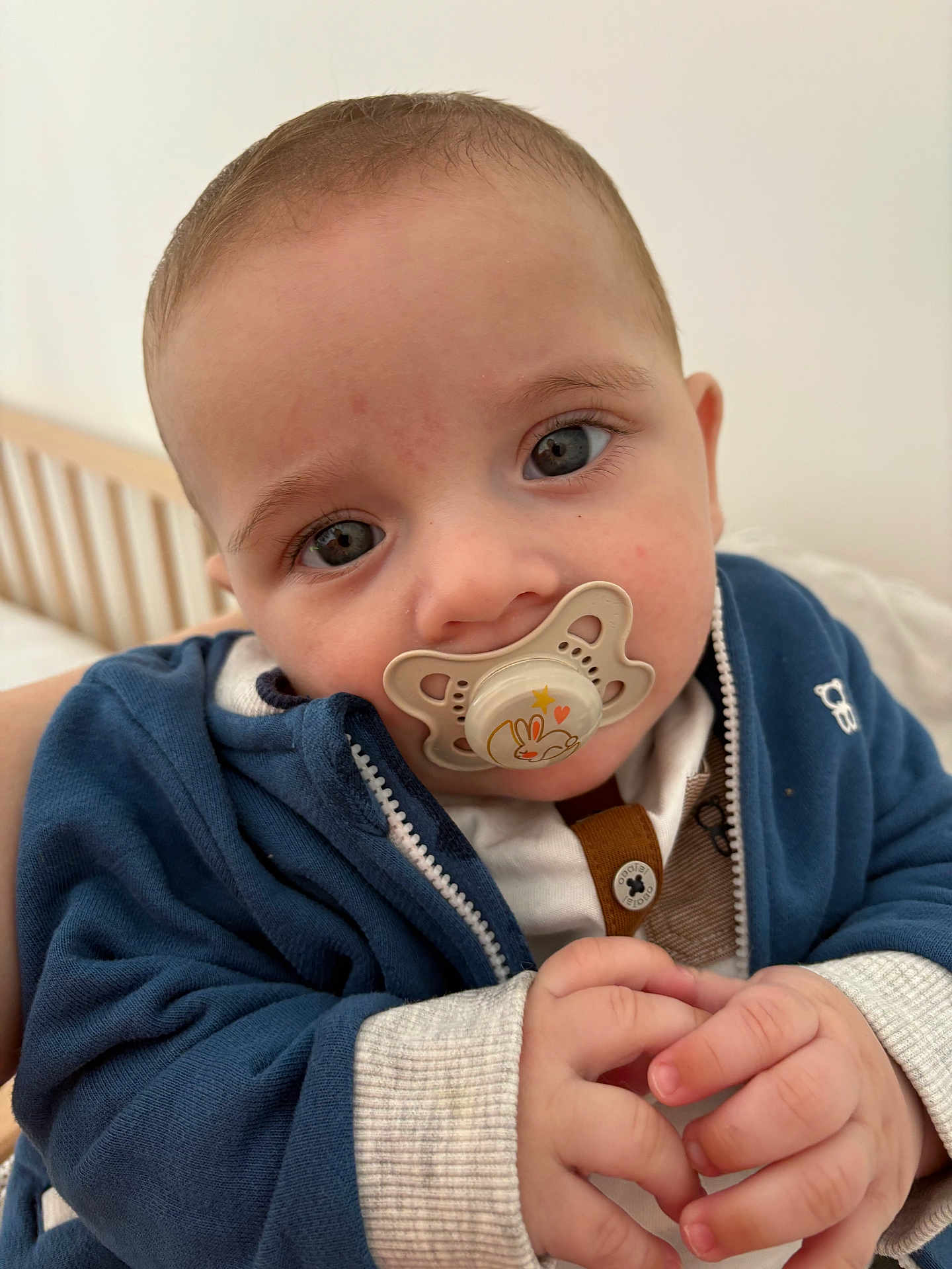 Mélio participe au concours pour gagner de l'argent avec cette photo : baby, pacifier, blue_jacket, hands, close_up, infant, cute, indoor, child, clothing, face, expression, portrait, person, skin, young, hoodie, sleepwear, bed, cradle