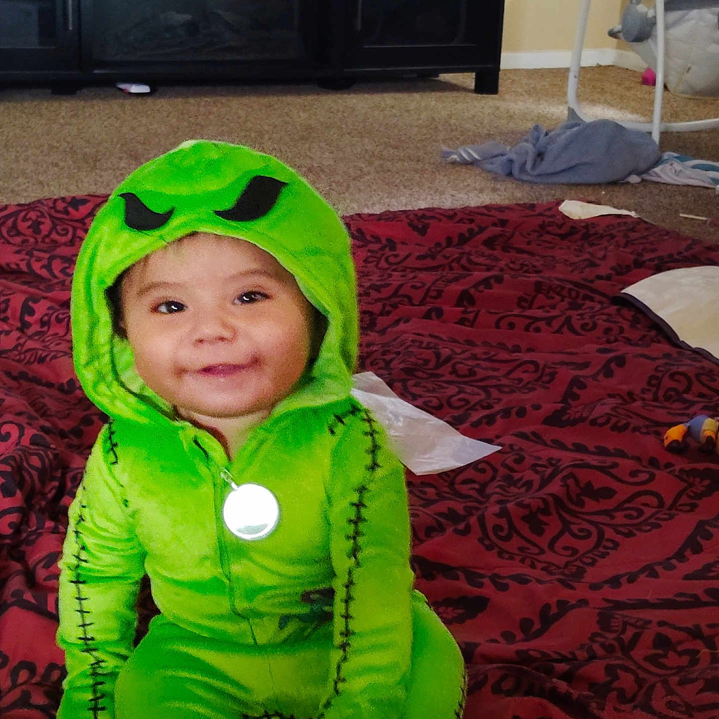 Davidson Flores joined the competition — help win amazing prizes! toddler, child, costume, green, smile, face, baby, sitting, blanket, pattern, indoor, carpet, toy, clothing, hood, pendant, furniture, home, baby_swing, cute