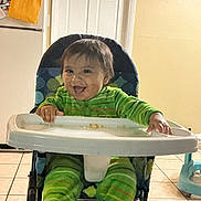 Davidson Flores joined the competition — help win amazing prizes! baby, high_chair, green_pajamas, smiling, kitchen, refrigerator, door, tile_floor, child, indoor, furniture, happy, person, seated, home, cute, infant, face, hands, playful