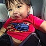child, toddler, baby, car_seat, car, portrait, smiling, face, eyes, hair, red_shirt, graphic_t_shirt, seatbelt, indoors, vehicle, close_up, sitting, happy, infant, photography