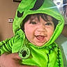 Promiseaity Flores joined the competition — help win amazing prizes! baby, black_hair, child, clock, costume, cute, face, green_clothing, hand, happy, holding, hood, indoor, infant, lens_flare, light, person, portrait, smile, wall