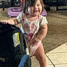 toddler, child, baby, smiling, happy, standing, indoors, living_room, stroller, baby_gear, carpet, tile_floor, toy, clothing, bodysuit, brown_hair, portrait, candid, home, daylight