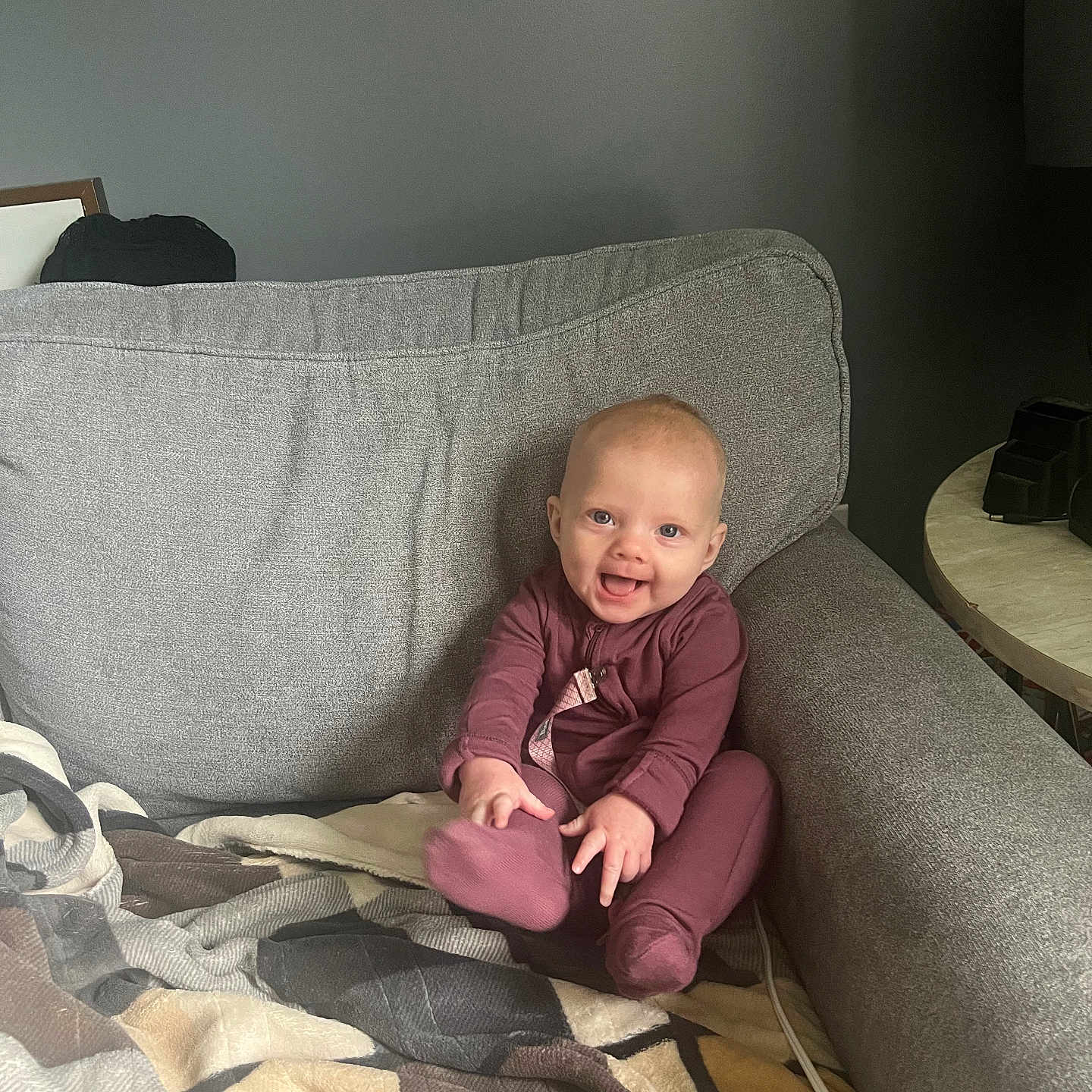 Bayleigh is registered to the contest to win money with this photo: baby, child, smiling, couch, blanket, indoors, onesie, happy, face, sitting, furniture, cozy, home, infant, person, cute, hands, foot, living_room, casual