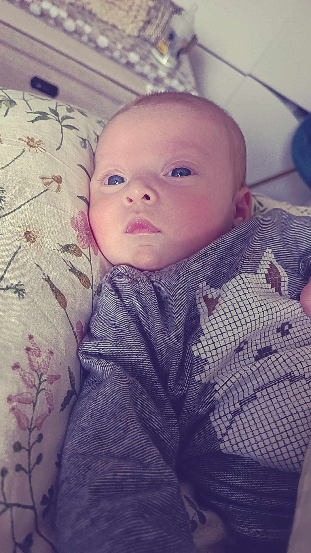 Priam a rejoint le concours — aidez-le/la à gagner de superbes lots ! baby, infant, face, blue_eyes, pillow, floral_pattern, clothing, striped, cute, portrait, indoors, child, soft_light, expression, young, person, head, lying_down, cozy, baby_outfit