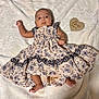 baby, infant, two_months, dress, floral_pattern, lace, blanket, wooden_sign, heart_shape, lying_down, cute, adorable, soft_texture, clothing, small_feet, face, portrait, child, newborn, indoors