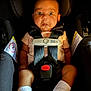 baby, car_seat, safety_harness, white_socks, pink_shirt, wide_eyes, surprised_expression, infant, child, seatbelt, black_background, head_support, evenflo, sensor_safe, infant_safety, child_safety, baby_clothing, cute, portrait, indoors