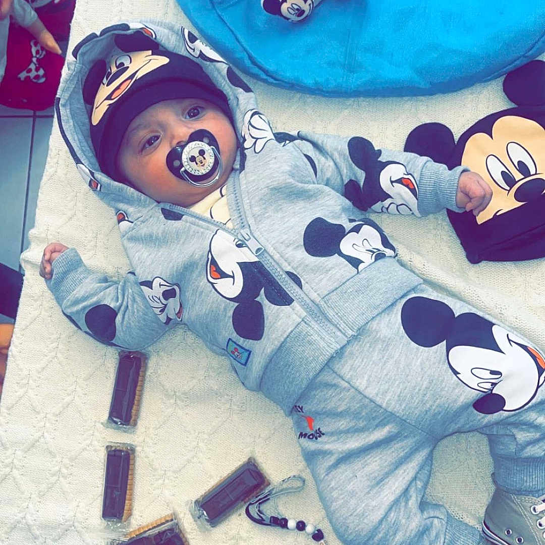 Emiliano a rejoint le concours — aidez-le/la à gagner de superbes lots ! baby, child, mickey_mouse, pacifier, hoodie, hat, blanket, toy, plush, shoes, floor, person, cute, clothing, indoor, accessories, pattern, lying_down, blue, gray