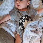 Tyler is registered to the contest to win money with this photo: baby, infant, onesie, converse, blanket, soft_texture, lying_down, curious, expression, indoor, couch, fabric, cozy, small_person, child, human, skin, head, face, foot