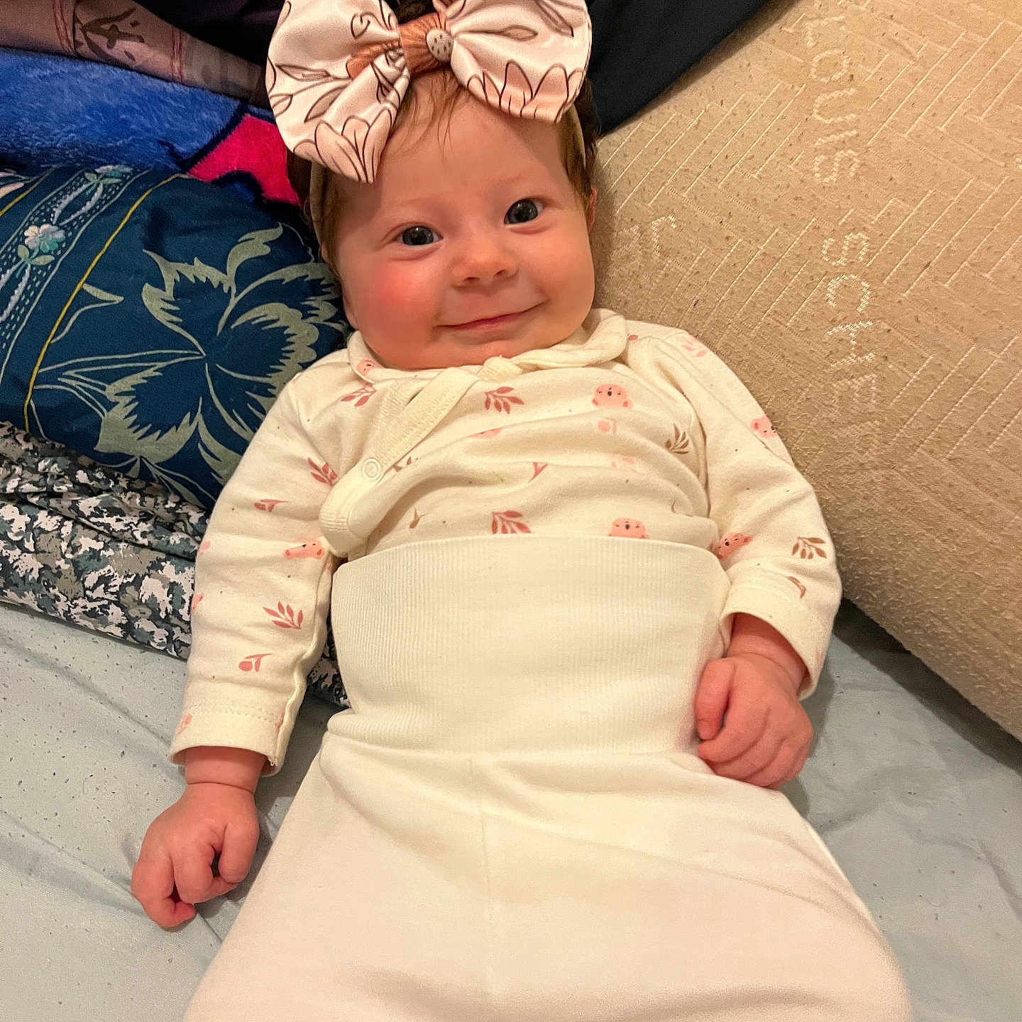 Mélona participe au concours pour gagner de l'argent avec cette photo : apparel, baby, bed, bow, cheerful, child, clothing, cute, fabric, face, hands, happy, headband, indoor, infant, lying_down, pillow, portrait, smiling, soft