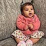 baby, child, pigtails, pink_sweater, floral_skirt, socks, couch, indoor, cute, infant, smiling, hands, face, person, seated, comfortable, home, adorable, young, portrait