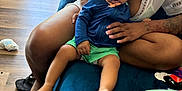 Nyuar is registered to the contest to win money with this photo: baby, child, woman, indoor, bucket_hat, blue_jacket, green_shorts, couch, wood_floor, vertical_blinds, hand, foot, person, seated, clothing, home, box, tattoo, skin, hat