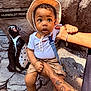 baby, child, hat, penguin, statue, tattoo, rock, sign, outdoor, curious, wide_eyes, holding, clothing, shorts, barefoot, person, animal_figure, nature, sunlight, portrait