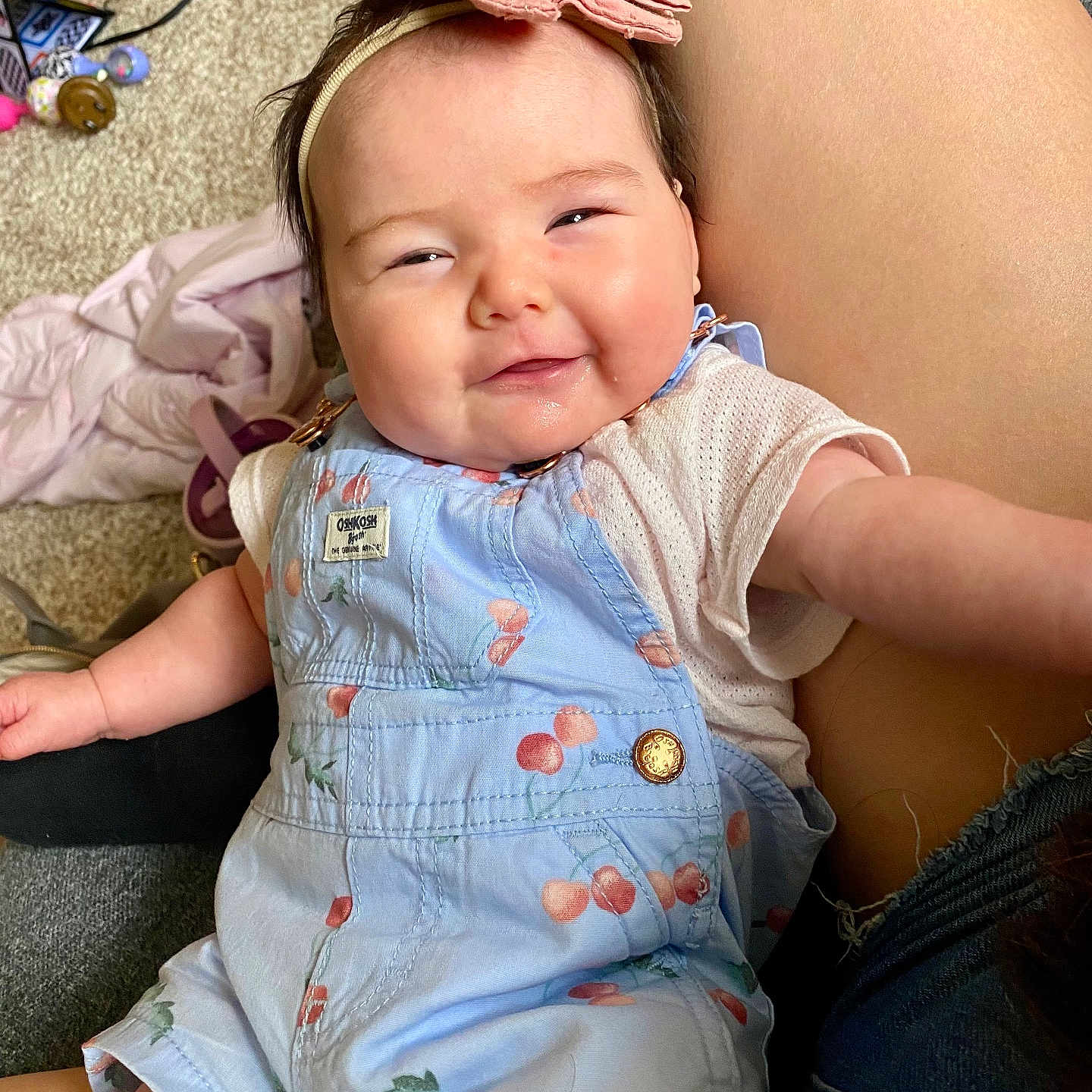 Kiara joined the competition — help win amazing prizes! baby, child, smiling, overalls, headband, pink_bow, cherry_pattern, sitting, indoor, carpet, person, skin, happy, cute, infant, clothing, portrait, hand, closeup, human