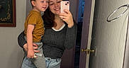 Treysen is registered to the contest to win money with this photo: bathroom, casual_clothing, child, door, happy, holding, indoor, mirror, phone, reflection, selfie, shorts, sink, smiling, toddler, towel_ring, toy, wall, woman, young_adult