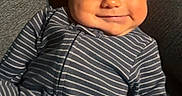 Jonah is registered to the contest to win money with this photo: baby, cheeks, child, comfort, couch, cozy, cute, face, gray, happy, indoors, infant, onesie, person, portrait, relaxing, seated, smile, striped_clothing, young_child