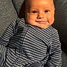 Jonah is registered to the contest to win money with this photo: baby, smile, onesie, striped_clothing, couch, gray, infant, child, happy, face, cheeks, comfort, seated, portrait, indoors, cozy, cute, young_child, person, relaxing