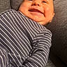 Jonah is registered to the contest to win money with this photo: baby, smile, striped_clothing, onesie, couch, gray, happy, infant, face, child, relaxing, comfort, indoors, portrait, young_child, cute, cheerful, skin, head, seated