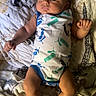baby, infant, onesie, puma, bed, blanket, patterned_sheet, sleepwear, person, skin, head, arms, legs, fists, indoors, soft_lighting, resting, cute, young_child, portrait
