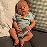 baby, infant, onesie, couch, pillow, blanket, indoor, furniture, person, child, seated, looking_at_camera, cute, soft_texture, relaxed, home, cozy, small, skin, head
