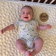 Emmett joined the competition — help win amazing prizes! baby, infant, crib, blanket, onesie, smiling, face, wooden_plaque, milestone, age_marker, cute, child, lying_down, happy, home, soft_texture, furniture, skin, person, newborn