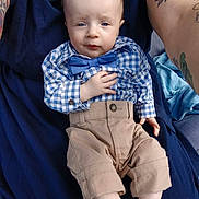 Coleson is registered to the contest to win money with this photo: baby, child, blue_shirt, bow_tie, beige_pants, tattoos, adult, lap, sitting, socks, person, portrait, indoor, clothing, cute, face, hands, expression, casual, closeup