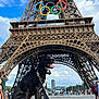 Floki a rejoint le concours — aidez-le/la à gagner de superbes lots ! dog, black_dog, eiffel_tower, olympic_rings, tourist, sky, cloud, landmark, outdoor, city, leash, sidewalk, people, architecture, travel, monument, happy, pet, summer, daytime