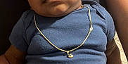 Idris joined the competition — help win amazing prizes! baby, child, infant, blue_onesie, necklace, jewelry, person, human, skin, arm, lap, sitting, close_up, indoor, casual_clothing, portrait, cute, young, calm, soft_lighting