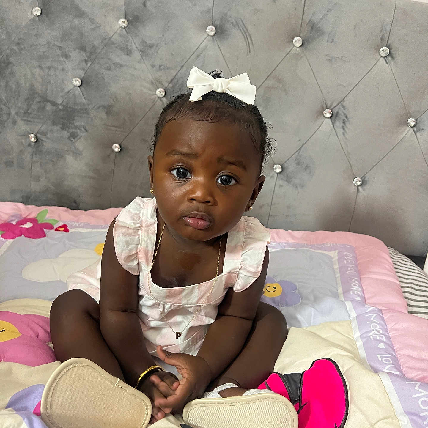 Paige is registered to the contest to win money with this photo: bed, black_hair, bow, bracelet, child, clothing, curly_hair, cute, expression, footwear, headboard, indoors, jewelry, necklace, pink, portrait, pouting, soft_toys, toddler, white