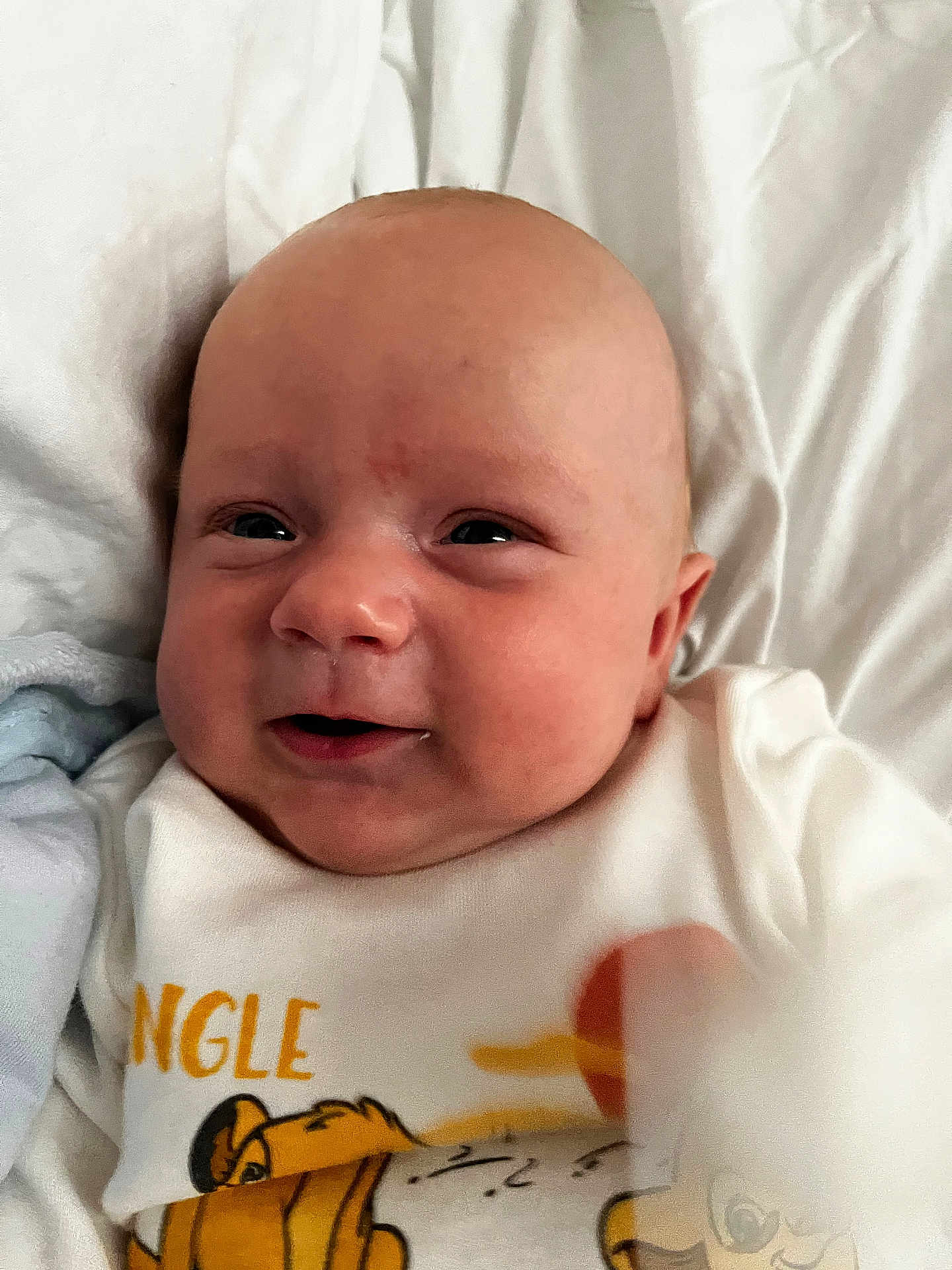 Lewis is registered to the contest to win money with this photo: baby, infant, face, smile, onesie, clothing, bed, blanket, cute, child, skin, head, portrait, sleepwear, young, lying_down, happy, indoors, soft, newborn