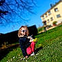 child, sunglasses, jacket, grass, flowers, doll, bouquet, outdoor, spring, sunny, greenery, house, blue_sky, person, crouching, casual_clothing, nature, daylight, young_child, playful