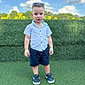 child, toddler, boy, portrait, outdoor, sunny, sky, clouds, sunflowers, hedge, grass, standing, sunglasses, shirt, shorts, sneakers, fashion, playground, daylight, smiling