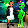 child, kid, dress, leather_jacket, black_boots, inflatable_alien, toy_knife, halloween, costume, face_paint, makeup, background, ufo, green, white_dress, black_choker, outdoor, sidewalk, plant_pot, playful