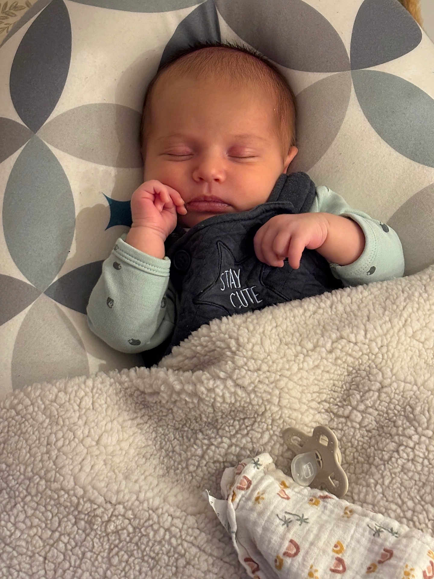 Albane participe au concours pour gagner de l'argent avec cette photo : baby, newborn, sleeping_baby, blanket, pacifier, onesie, swaddle_blanket, hand, face, closed_eyes, bedding, nursery, patterned_pillow, cozy, infant_clothing, embroidered_text, small_hand, peaceful, soft_texture, sleeping