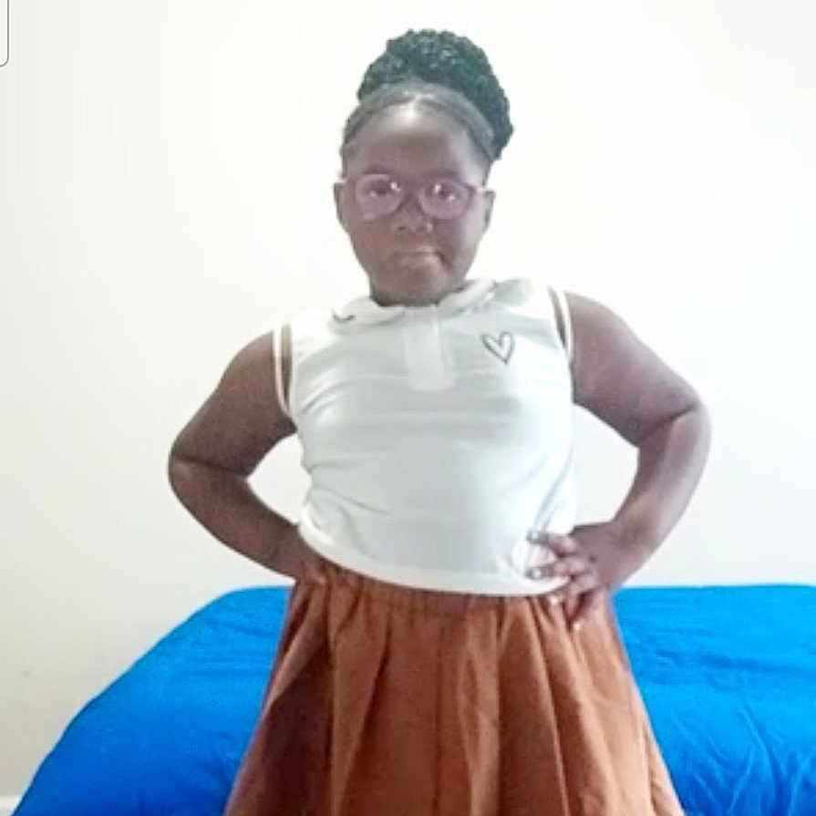 Saraya is registered to the contest to win money with this photo: child, girl, portrait, standing, indoors, bedroom, bed, blue_bedspread, skirt, white_shirt, glasses, braided_hair, hands_on_hips, confident, fashion, full_body, posing, wall, smartphone_screenshot, home