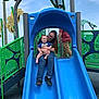 Ashton is registered to the contest to win money with this photo: baby, woman, slide, playground, outdoor, smiling, child, person, clothing, glasses, jeans, blue, green, playstructure, happy, sky, fun, recreation, park, adult