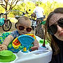 baby, sunglasses, woman, man, dog, outdoor, toy, activity_center, bicycle, tree, person, playful, pout, face, sunlight, summer, greenery, casual, family, fun