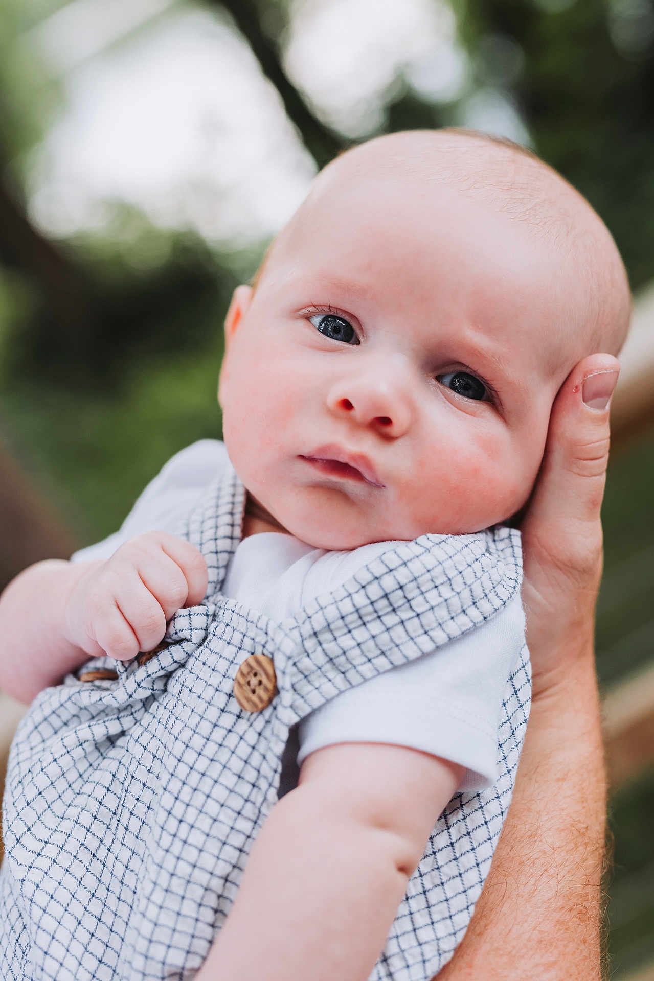 Waylon is registered to the contest to win money with this photo: baby, infant, child, face, hand, clothing, overalls, white_shirt, outdoor, nature, greenery, portrait, cute, expression, skin, human, person, holding, blurred_background, closeup