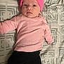 baby, infant, newborn, pink_hat, pink_sweater, black_pants, white_socks, bed, blanket, patterned_bedding, pillow, lying_down, portrait, face, eyes, cute, one_person, indoors, infant_clothing, baby_photo